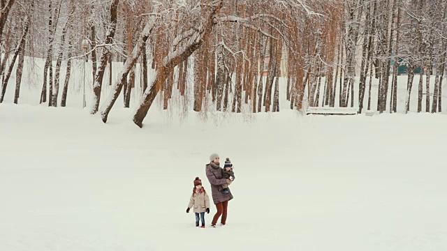一位年轻的母亲和她的孩子们站在白雪覆盖的公园里