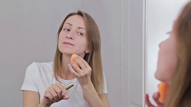 美丽的年轻女子使用遮瑕粉底霜化妆。
