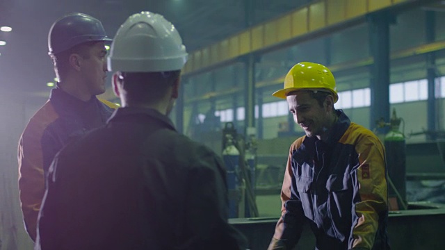 一群戴着安全帽的重工业工人正在一家工厂里谈话。