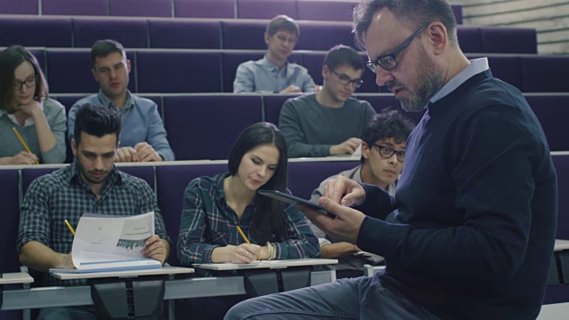 一位大学教授正在给一群来自不同民族的学生上课，他正在检查一台平板电脑。