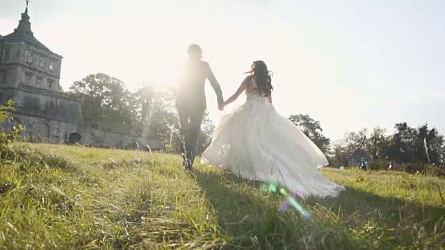 在日落城堡附近的草地上奔跑的新婚夫妇