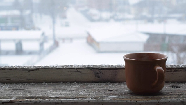 雪花落在旧木窗台上的杯子上