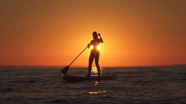 慢动作:健康的年轻女性骑手站起来划桨在金色的日落