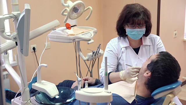 女牙医在牙科诊所给男病人做手术，特写。健康的概念