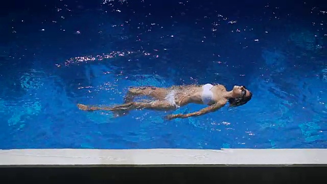 详情图-穿着白色比基尼的可爱女人在水里游泳。小女孩在游泳池里飘浮着，显得舒适而愉快。一个快乐美丽的女性游客在度假胜地放松的特写