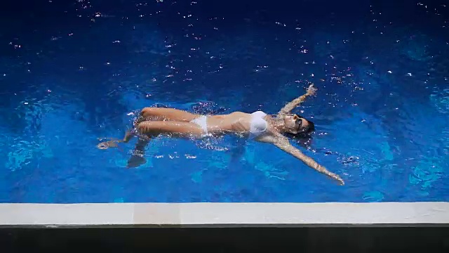 详情图-穿着白色比基尼的可爱女人在水里游泳。小女孩在游泳池里飘浮着，显得舒适而愉快。一个快乐美丽的女性游客在度假胜地放松的特写