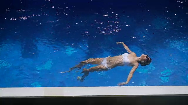 详情图-穿着白色比基尼的可爱女人在水里游泳。小女孩在游泳池里飘浮着，显得舒适而愉快。一个快乐美丽的女性游客在度假胜地放松的特写