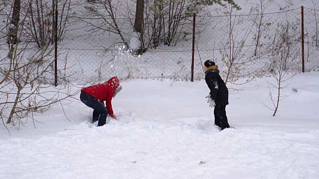 母亲和儿子吐出柔软的，新鲜的雪。一个女人和一个十几岁的男孩正在庆祝冬天。公园里一个多云的冬日。缓慢的运动。