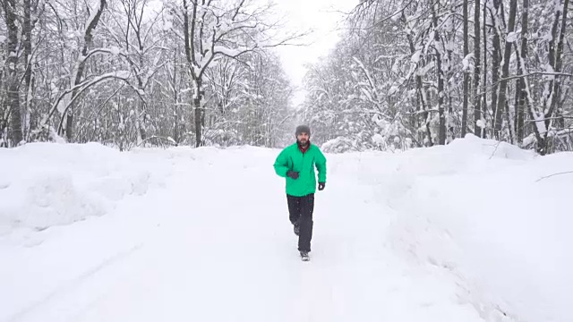 一名蓄着胡子的成年男子在暴风雪中跑步。在雪地里奔跑的运动员。冬日森林里的独行者。从前面的慢动作投篮