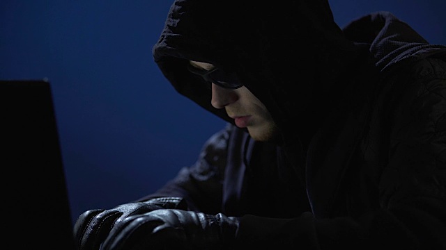 穿着黑衣，戴着墨镜和手套的奇怪男子正在从笔记本电脑中窃取数据