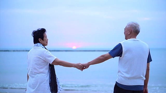 相爱的亚洲老年夫妇在海上日出快乐地在一起