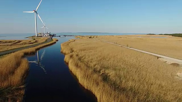 4 k。飞越蓝色的河流和田野，向风力涡轮机靠近大海，鸟瞰图。