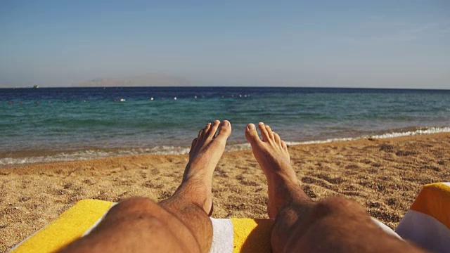 男人的腿躺在海滩太阳躺椅附近的大海