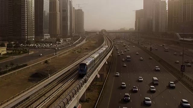 从空中俯瞰蓝色的高速列车，它穿过高速公路上的立交桥，汽车被摩天大楼包围。迪拜,阿联酋