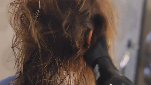 专业美发师使用吹风机。年轻女子在美发沙龙做头发。男性造型师拿着吹风机。理发师和吹风机。叠加。理发师在起作用。美容沙龙