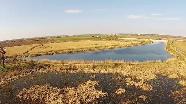 飞越具有特定栖息地的天然沼泽，背景为人工池塘边缘和农业景观，鸟瞰图