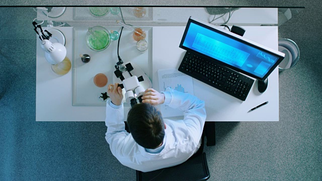 一个科学家观察显微镜和分析信息与计算机的顶视图。