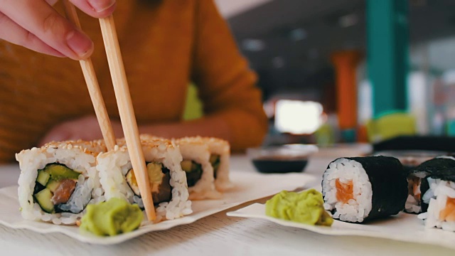 女孩坐着用木棒在咖啡馆的桌子上拿着一个寿司是寿司，日本料理