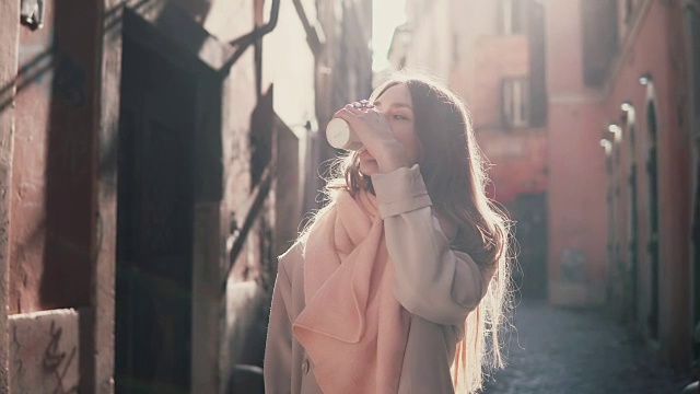 年轻时尚的女人在早晨环顾四周的肖像。快乐的女孩在古老的街道上漫步，喝着咖啡