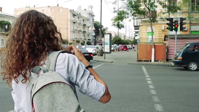 一头卷发背着双肩包的苗条女子在人行横道等待绿灯