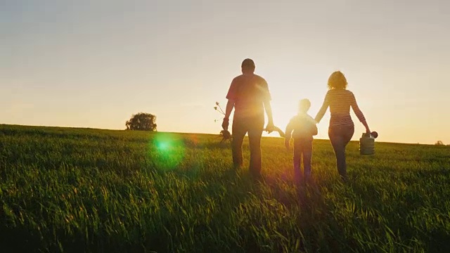 詳情圖-后視圖:一個(gè)友好的家庭和一個(gè)年幼的兒子打算種樹。攜帶幼苗，鏟子和噴壺。落日背景下美麗田野的剪影