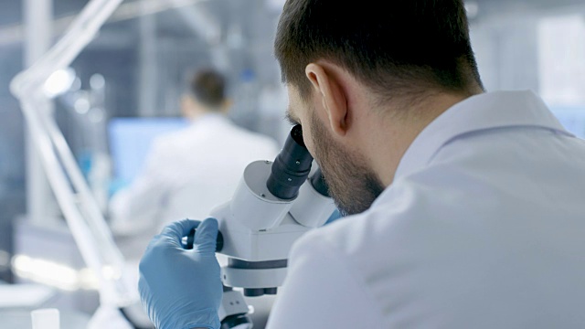从一个研究科学家的肩膀看显微镜。他和他的同事在现代实验室进行实验。