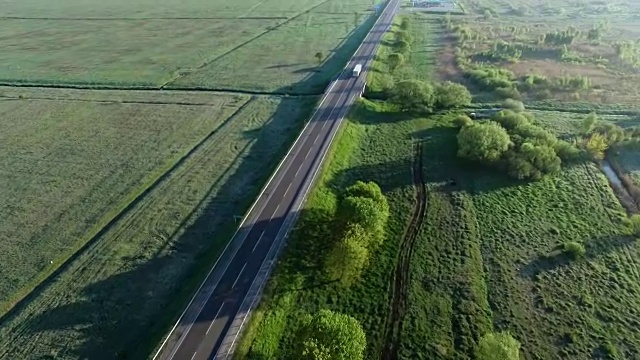 詳情圖-一輛卡車在太陽升起的綠色田野之間的道路上行駛的全高清航拍鏡頭