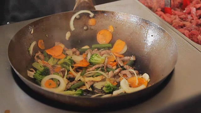 在街头美食节上油炸蔬菜和肉类的专业厨师。用牛肉和蔬菜炒近。烹饪的过程