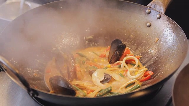在街头美食节上，专业厨师正在用蔬菜煎贻贝和虾。烤虾和软体动物近距离。海鲜的烹调过程。传统的亚洲食物