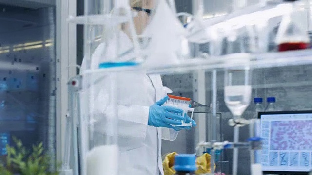年轻女科学家带着试管在繁忙的实验室里行走的后续镜头。不同年龄的男性和女性科学家在这个国家的艺术实验室工作。