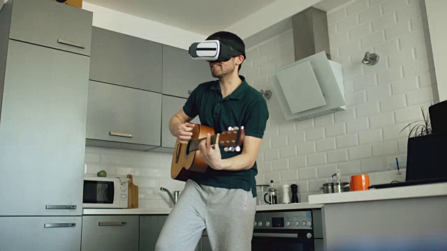 快乐的年轻人在厨房用VR 360耳机跳舞和弹吉他，感觉他在家里的音乐会吉他手