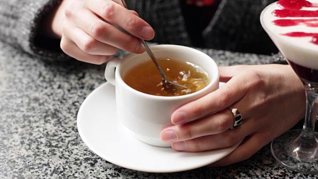 女孩在白杯子里搅拌糖。女性的手与一杯茶的特写。