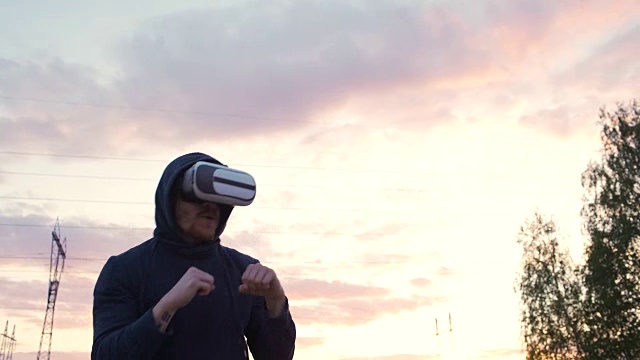 詳情圖-剪影的年輕男子拳擊手在VR,360耳機(jī)訓(xùn)練踢在城市公園日落在虛擬現(xiàn)實(shí)戰(zhàn)斗