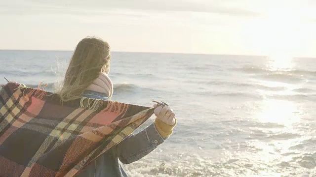 自由:年轻女子站在海边，手举格子。快乐的女性在寒冷的刮风的一天在海滩上