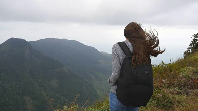 年轻的女游客背包欣赏美丽的风景在山。女游客站在美丽的峡谷边缘，欣赏大自然。慢镜头