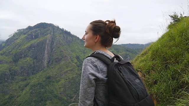 年轻的女游客背包欣赏美丽的风景在山。女游客站在美丽的峡谷边缘，欣赏大自然。慢镜头