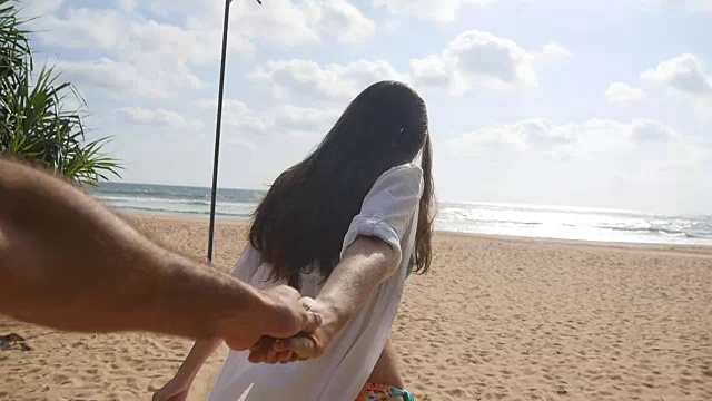 女孩牵着男人的手，在热带异国的海滩上奔向大海。跟着我拍的一个年轻女人拉着她的男朋友在海边。暑假或假期。的观点。观点慢动作