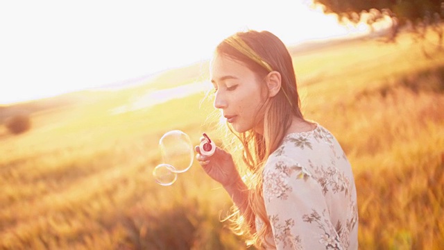 美丽的复古风格的女人吹泡泡在金色的麦田