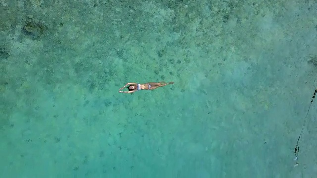 鸟瞰图一个迷人的女人在比基尼漂浮在水晶清澈的海洋。一个美丽的女孩在印度洋游泳