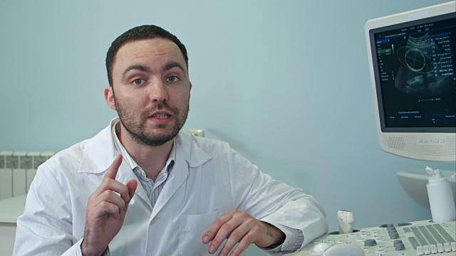 年轻男医生坐在超声波扫描机旁边对着摄像头说话