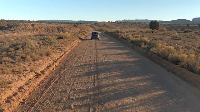 镜头:日落时分，一辆黑色吉普车在尘土飞扬的道路上行驶，穿过干燥的平原