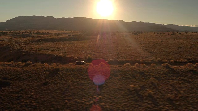 镜头:金色的夕阳下，一辆黑色SUV行驶在沙漠山谷尘土飞扬的道路上