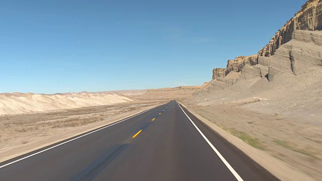 FPV:驾驶沿着空的道路通过灰色的沙漠峡谷在犹他州，美国