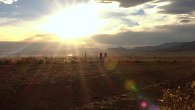 慢镜头近景:金色的夕阳下，一辆黑色SUV行驶在尘土飞扬的砾石路上