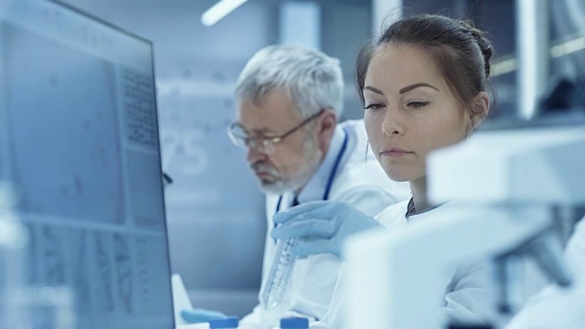 医学研究科学家看试管结果和类型提取的数据到她的电脑。科学家在现代实验室工作。