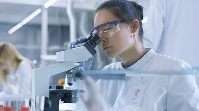 医学研究科学家检查实验室小鼠和在显微镜下观察组织样本。她在一个灯光实验室工作。
