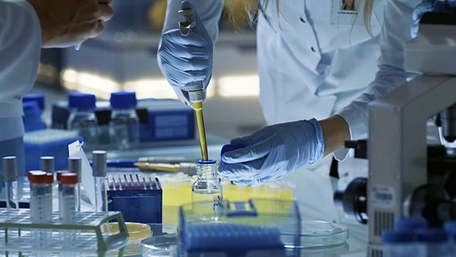 女研究科学家使用微管填充试管。科学家在一组科学家试图治愈致命的疾病，他们在一个大实验室/研究中心工作。