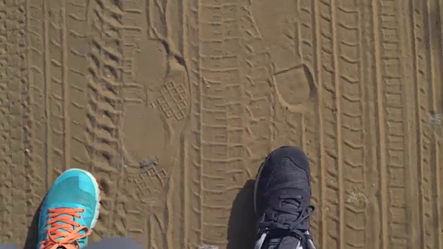 一个旅行者的腿。运动的双腿躺在荒芜的路上。沙地上有汽车轮胎的痕迹。在旅途中主动休息。徒步旅行