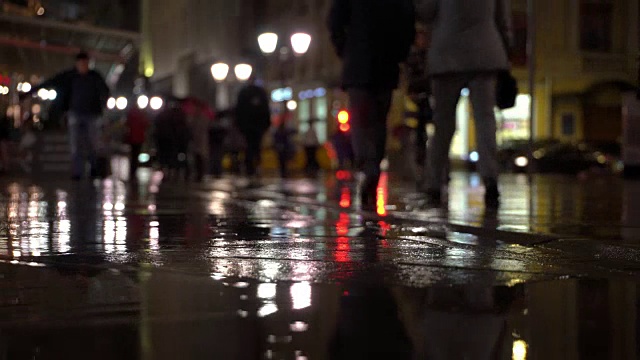 雨夜，在路灯的照耀下，雨点落在五颜六色的沥青上。不认识的人在雨伞下走，过有红绿灯的马路。美丽的彩色的散景。天气、交通、城市街道、现代城市生活方式的概念