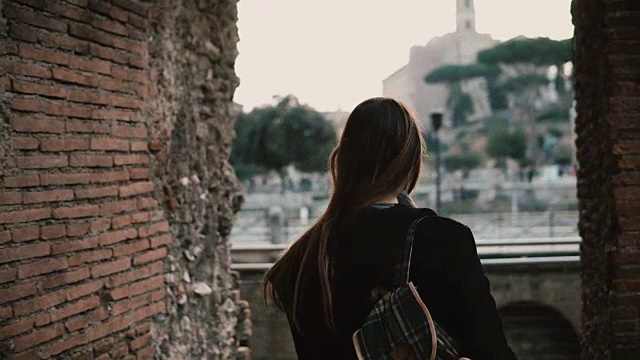 一名穿着黑色外套的女游客正走过罗马广场的桥。女孩对意大利古罗马古城感到兴奋